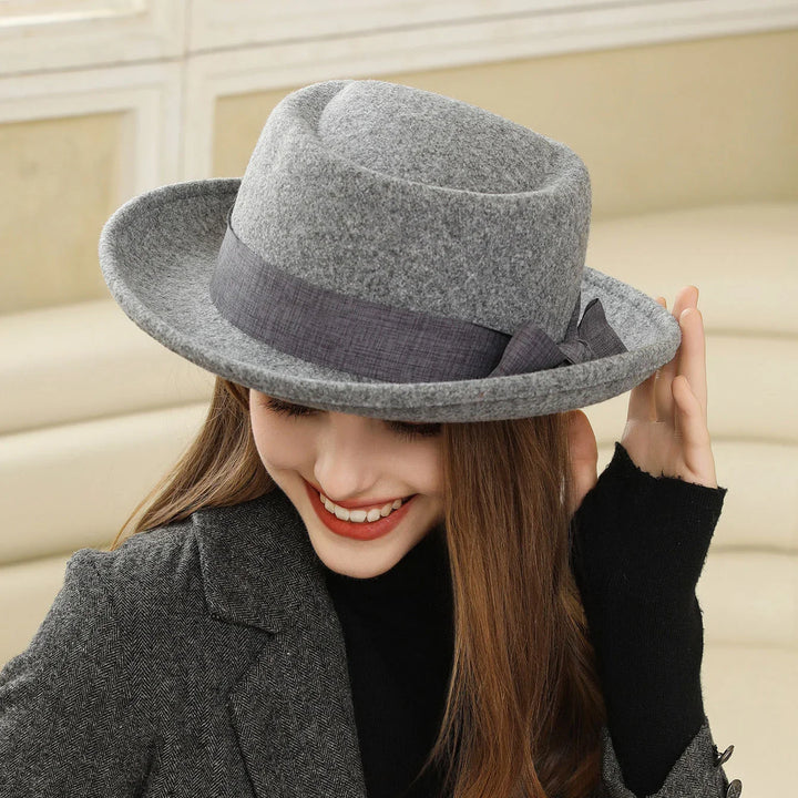 Smiling woman wearing stylish grey felt fedora hat with dark ribbon, grey blazer, and black top