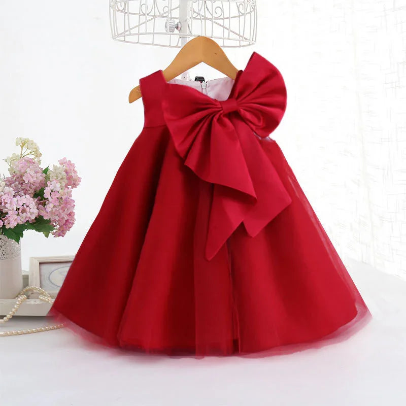 Elegant red sleeveless toddler dress with large bow on shoulder, displayed on wooden hanger