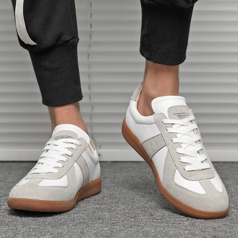 Close-up of white and beige casual sneakers with gum sole worn with black pants on gray floor