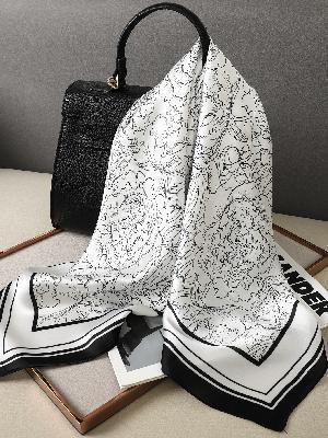 Black textured handbag with black and white abstract patterned silk scarf draped on beige surface
