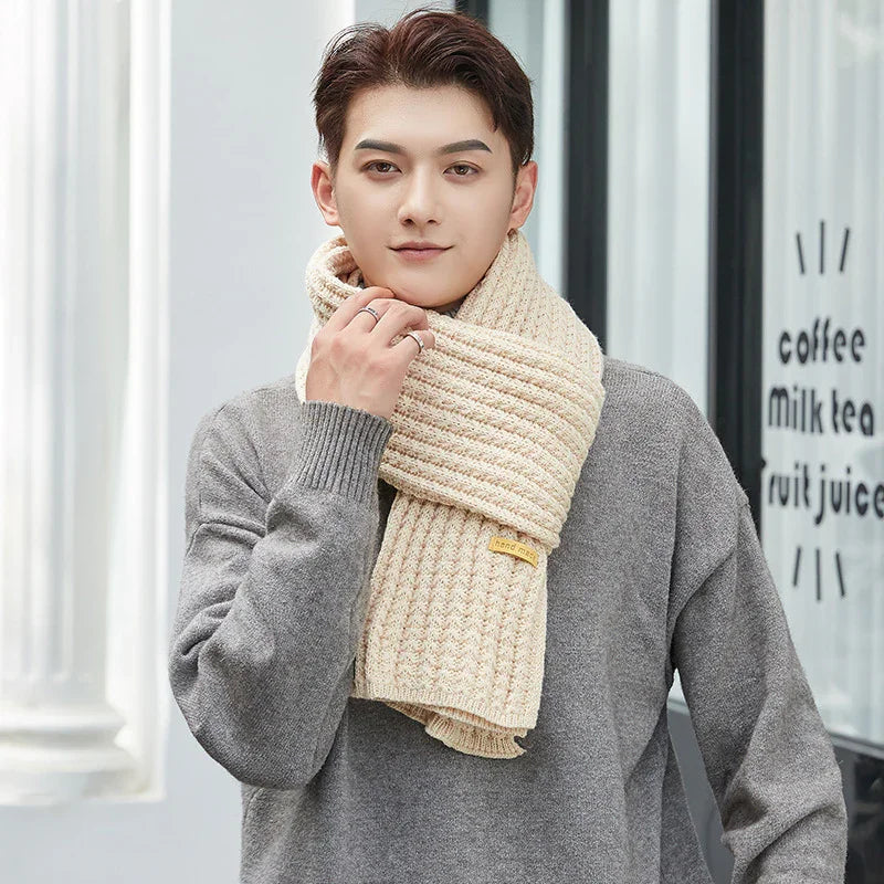Young man wearing beige knitted scarf and gray sweater standing outdoors by cafe window
