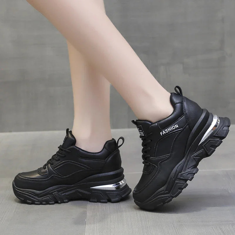 Black chunky platform sneakers with silver accents and FASHION logo on model feet on gray floor
