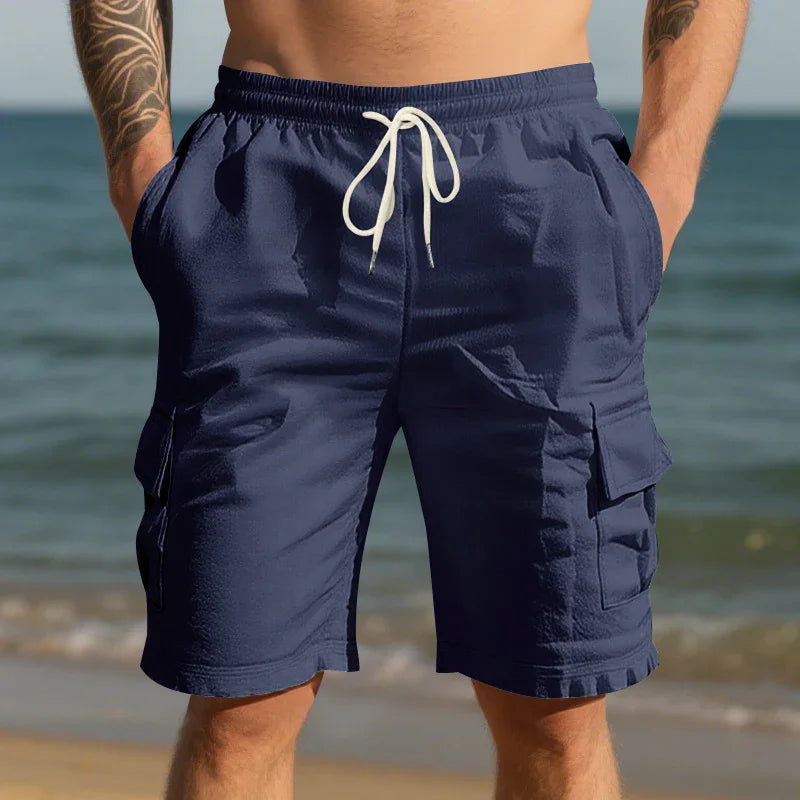 Man wearing navy blue cargo swim shorts with white drawstring at beach shore