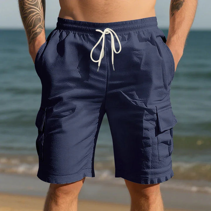 Man wearing navy blue cargo swim shorts with white drawstring at beach shore