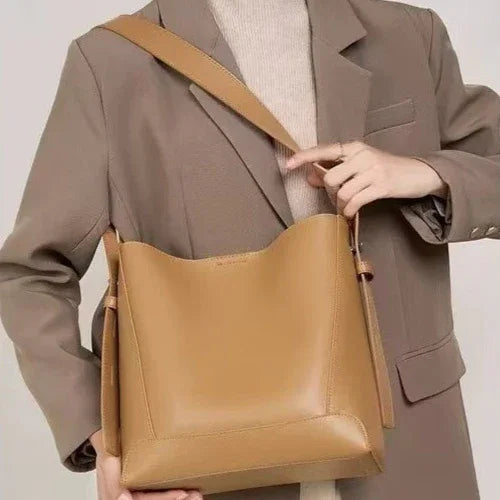 Woman wearing beige coat and sweater holding a large tan leather shoulder bag