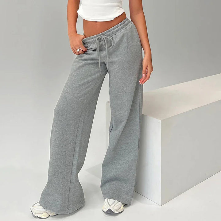 Woman wearing loose grey sweatpants with drawstring and white sneakers in minimalist setting