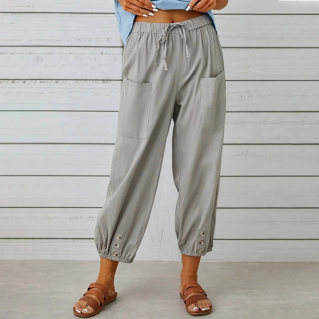 Woman wearing light gray drawstring pants with pockets and button details at ankles