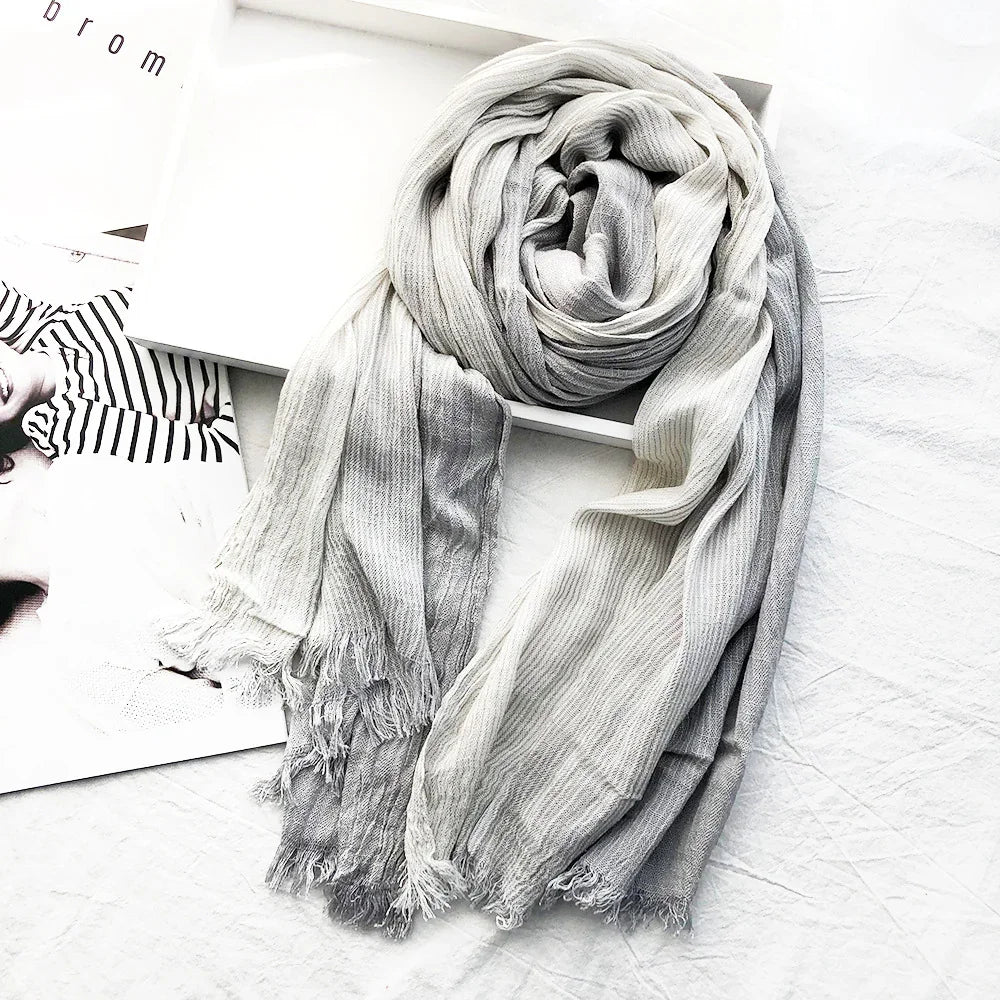 Soft ribbed ombre scarf in shades of gray and white with fringed edges on a white surface