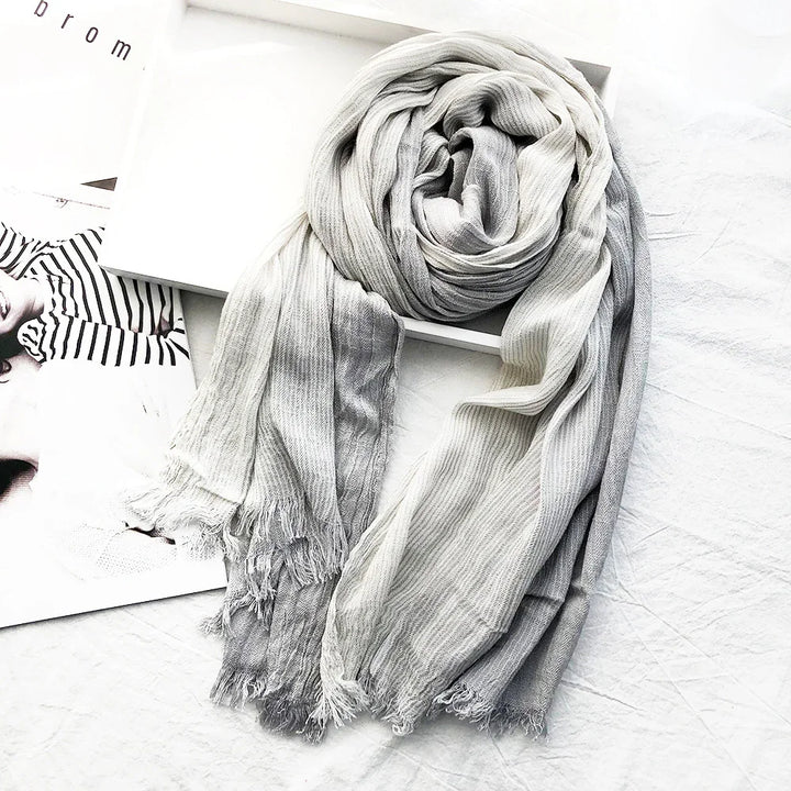Soft ribbed ombre scarf in shades of gray and white with fringed edges on a white surface