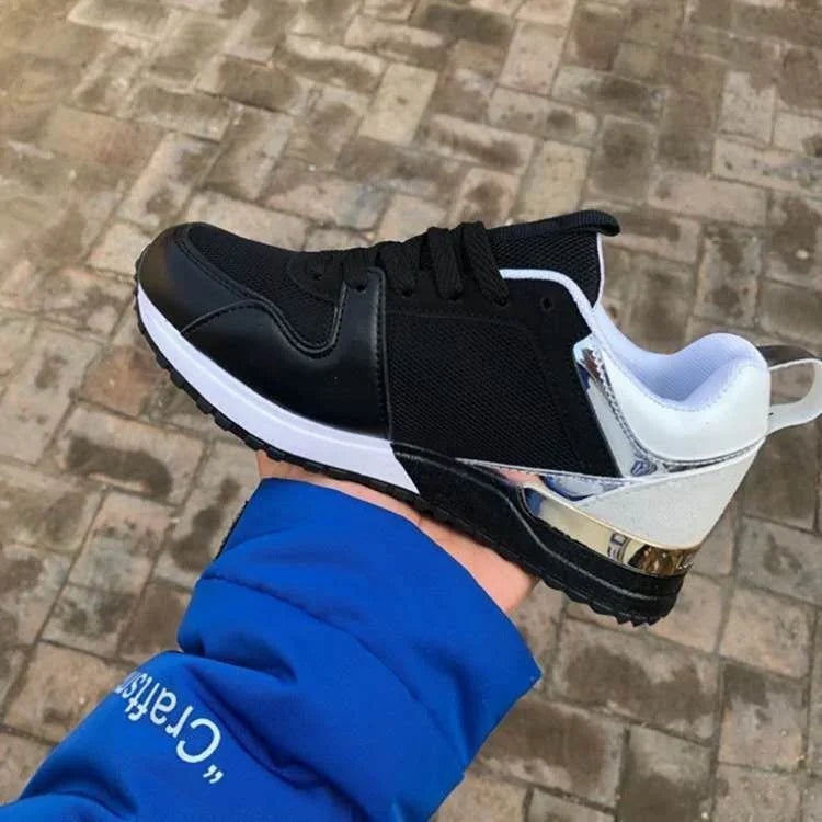 Black and white athletic sneaker with metallic silver heel detail held over outdoor brick pavement
