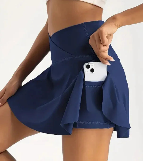 Woman wearing navy blue athletic skort with side pocket holding a white smartphone against white background