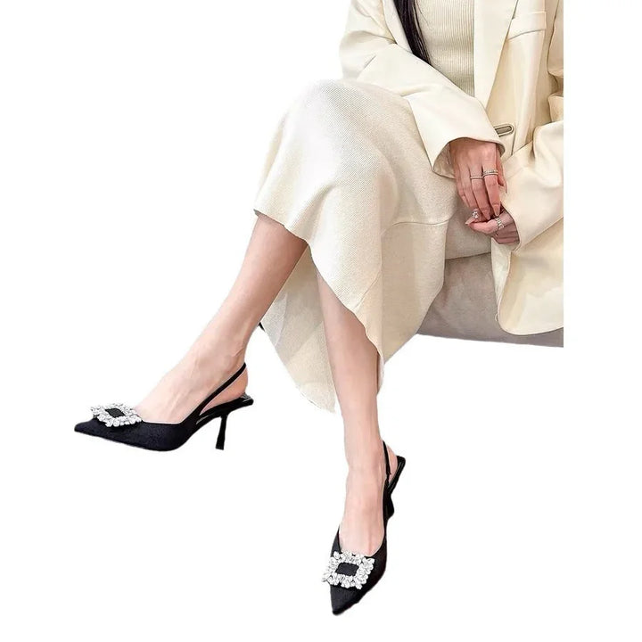 Woman wearing beige skirt and blazer with black slingback heels featuring rhinestone buckles