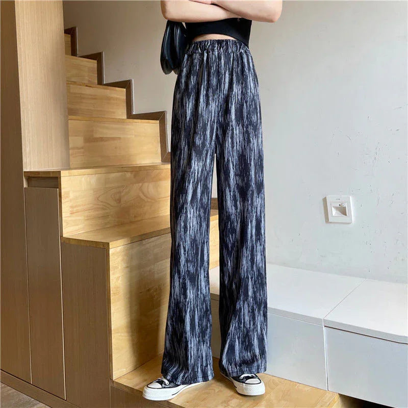 Person wearing black and gray patterned wide-leg pants and black sneakers standing near wooden stairs
