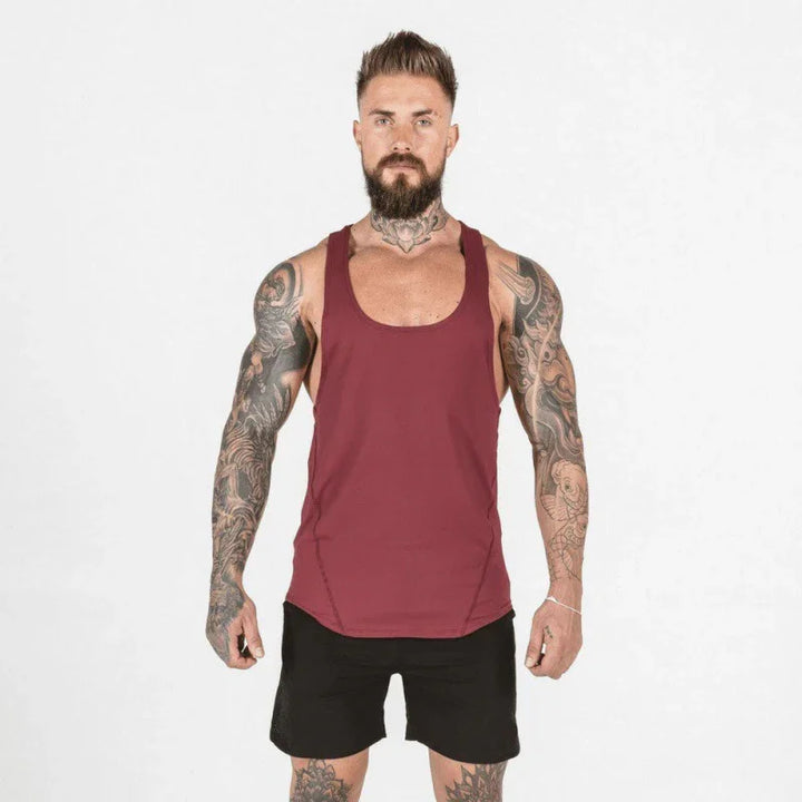Tattooed muscular man wearing maroon tank top and black shorts against white background