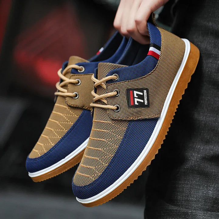 Hand holding stylish casual sneakers with blue and brown fabric and gum soles