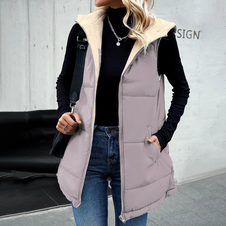 Woman wearing light gray puffer vest with cream fleece lining, black turtleneck, blue jeans, and silver necklace
