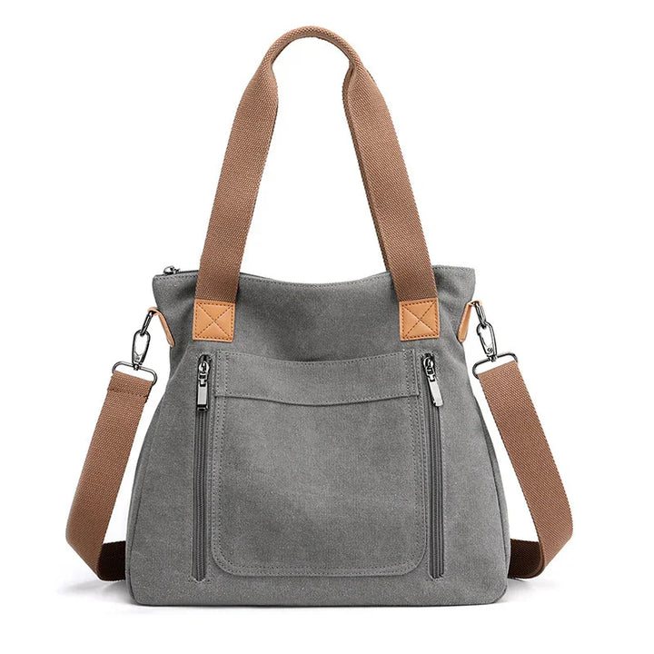 Grey canvas tote bag with brown handles and detachable shoulder strap, front zip pockets