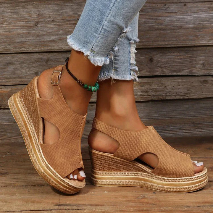 Brown wedge sandals with cutout design worn with light ripped jeans and green beaded ankle bracelet on wooden floor