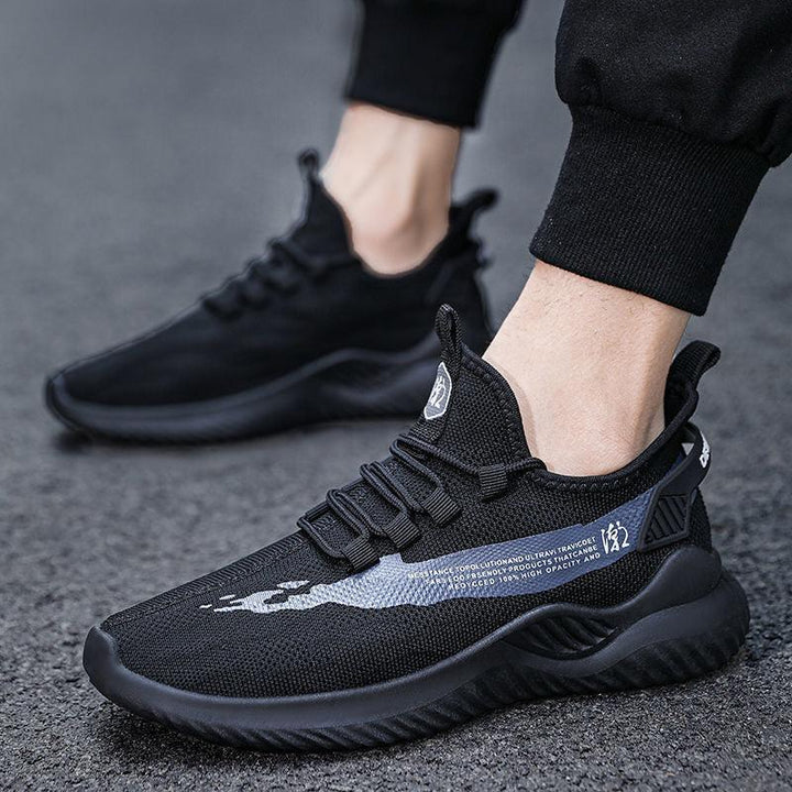 Close-up of black knit sports sneakers with dark blue pattern worn with black jogger pants on asphalt