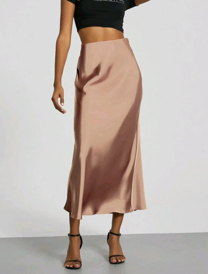 Woman wearing a beige satin midi skirt paired with black strappy sandals and a cropped black top