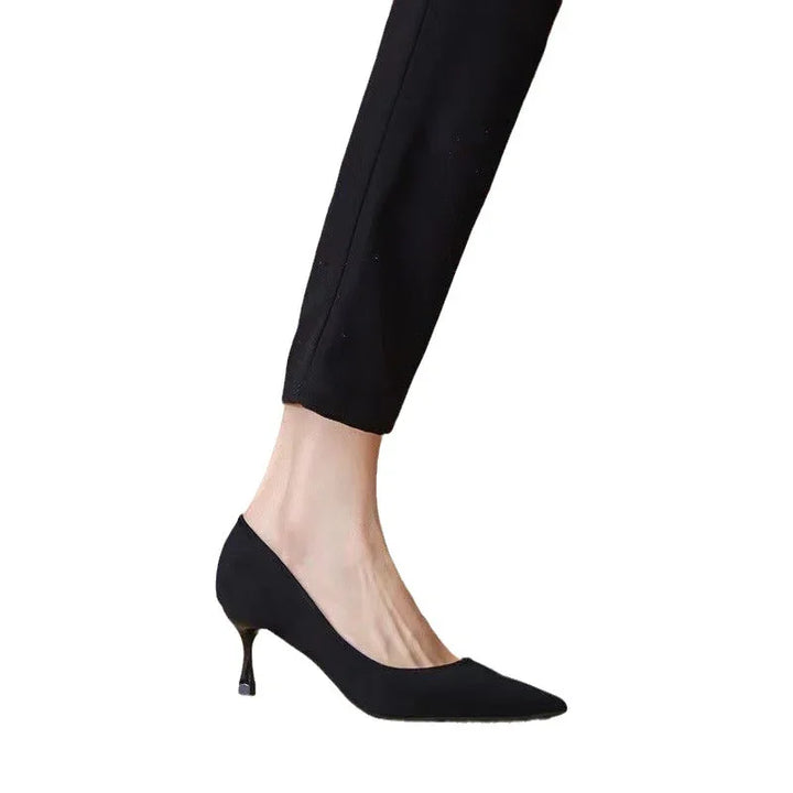 Woman wearing black pointed-toe kitten heel shoes with slim black pants on white background