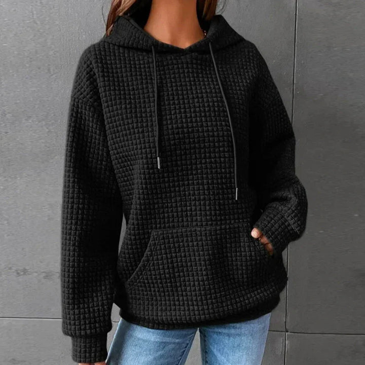 Black waffle knit hoodie with kangaroo pocket worn with blue jeans against gray wall