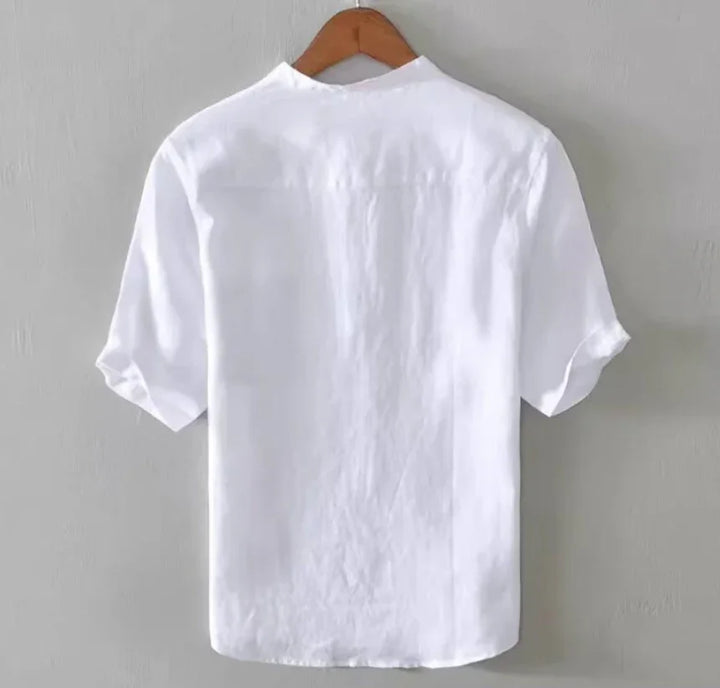 Back view of a plain white short-sleeve shirt hanging on wooden hanger against gray wall