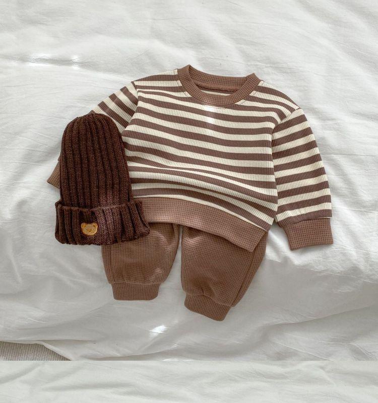 Brown and beige striped toddler sweater, matching brown pants, and a dark brown knit beanie with bear patch on white fabric