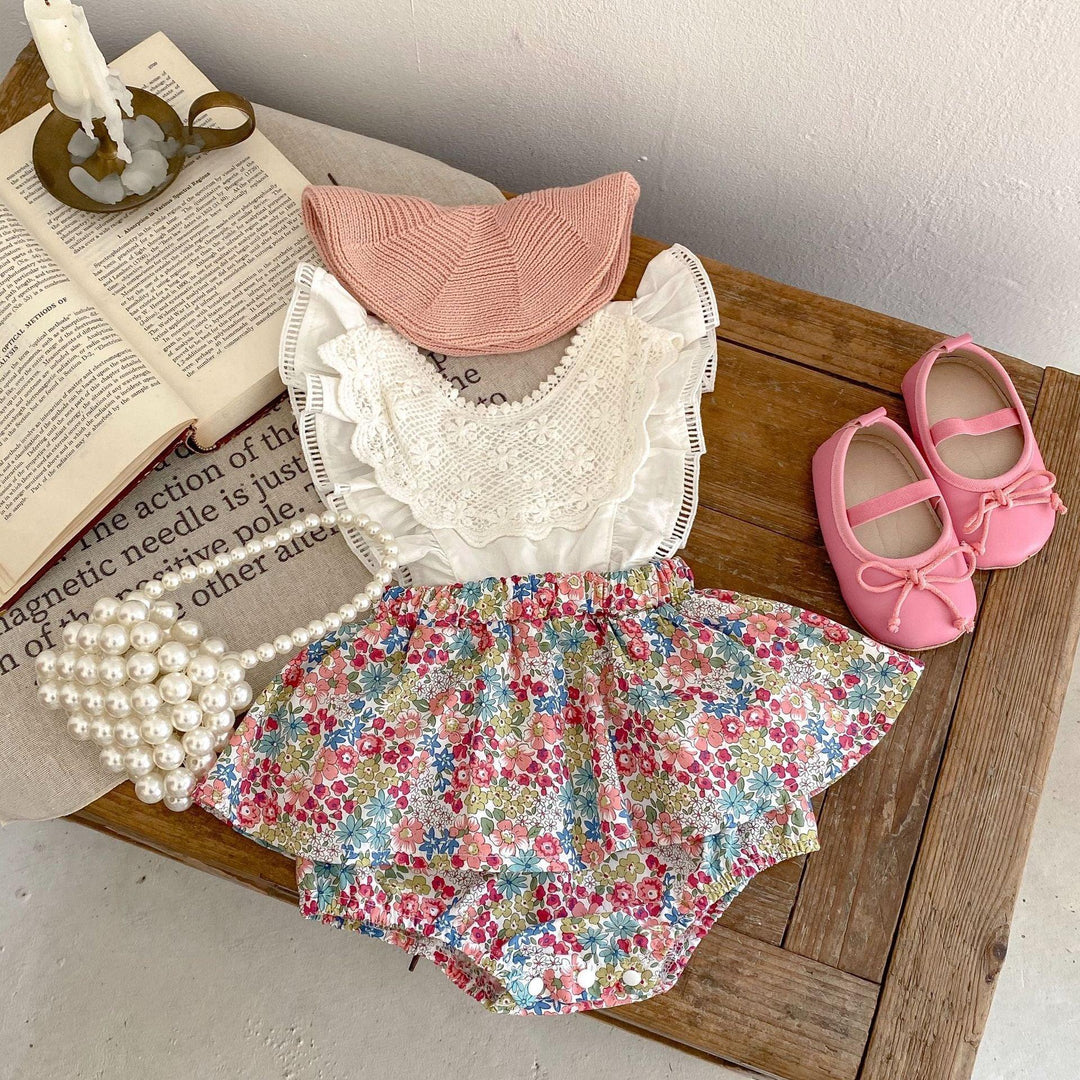 Cute baby outfit with floral romper, white lace top, pink knit hat, pink shoes, and pearl bag on wooden table