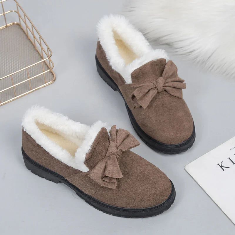 Brown suede winter loafers with white faux fur lining and decorative bows on gray surface