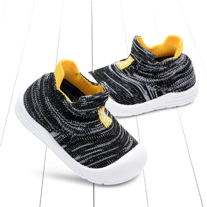 Black and white knit toddler sneakers with yellow inner lining and white rubber soles on white wood floor