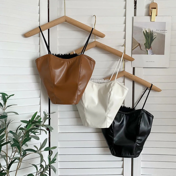 Brown, white, and black faux leather corset tops hanging on wooden hangers against white shutter backdrop