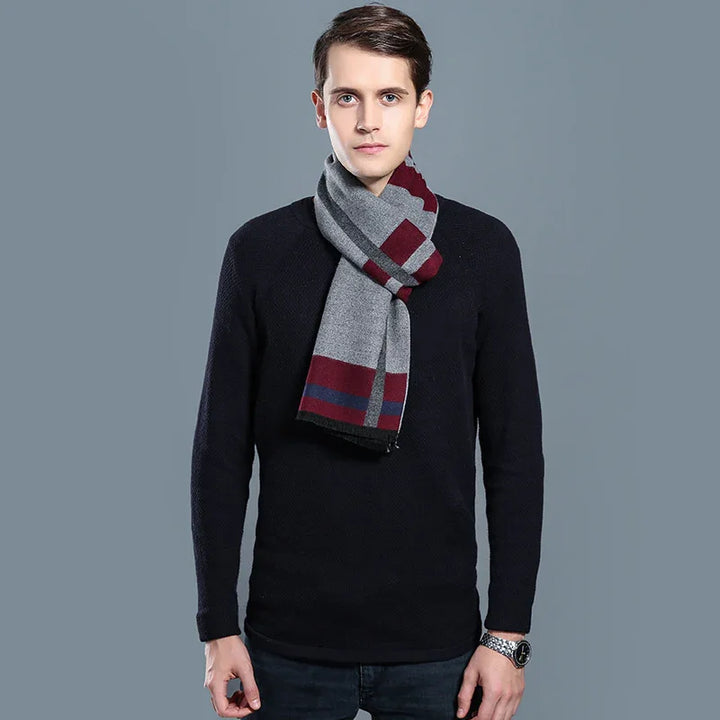 Young man wearing black sweater, gray and burgundy striped wool scarf, and wristwatch on gray background