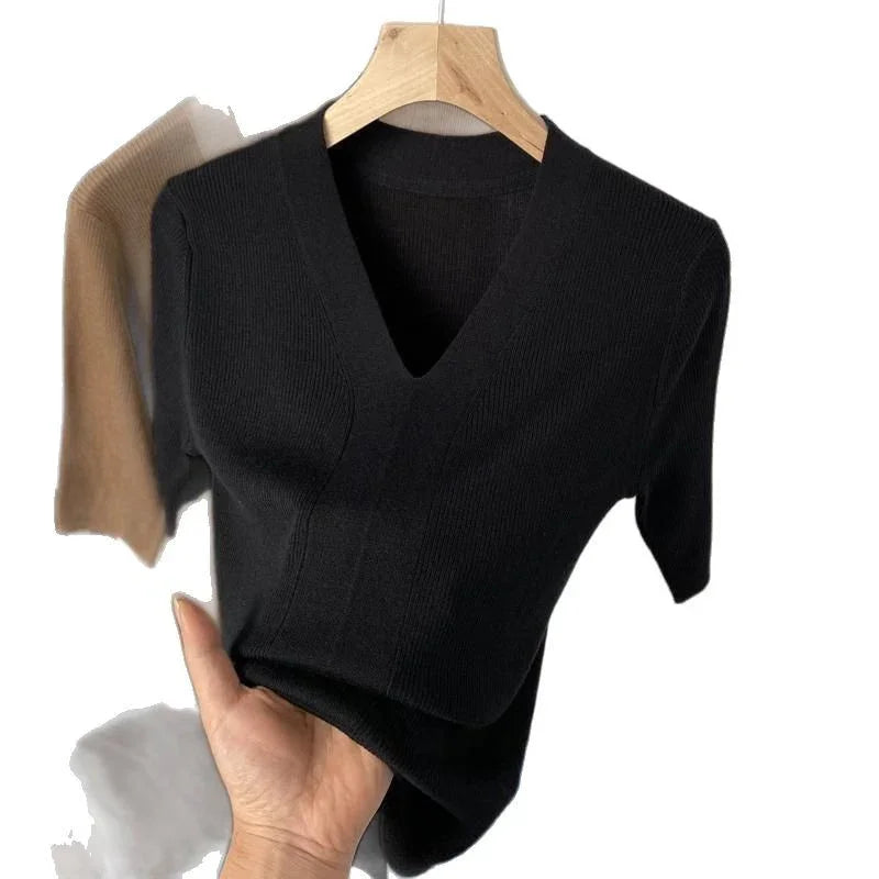 Hand holding black knit V-neck short sleeve top on wooden hanger with beige top in background