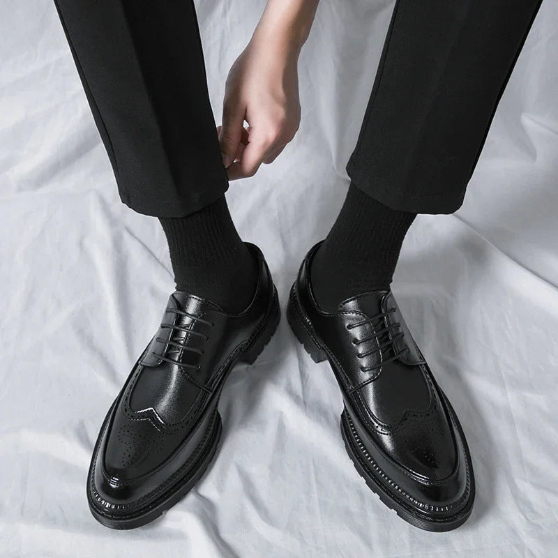 Person wearing black leather brogue dress shoes with black socks and black pants on white fabric