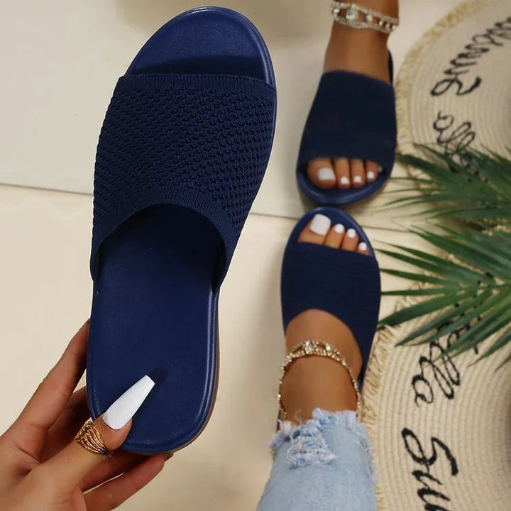 woman wearing and holding navy blue knit slide sandals with ankle bracelets and white nail polish