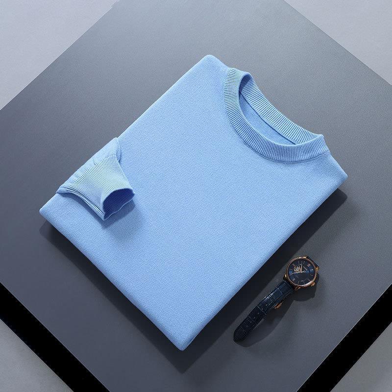 Light blue folded sweater with ribbed collar and cuff next to black leather strap wristwatch on gray surface