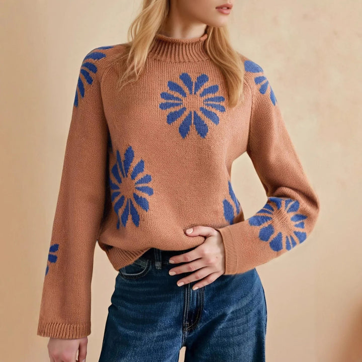 Woman wearing brown knitted sweater with blue flower patterns and blue jeans against beige background