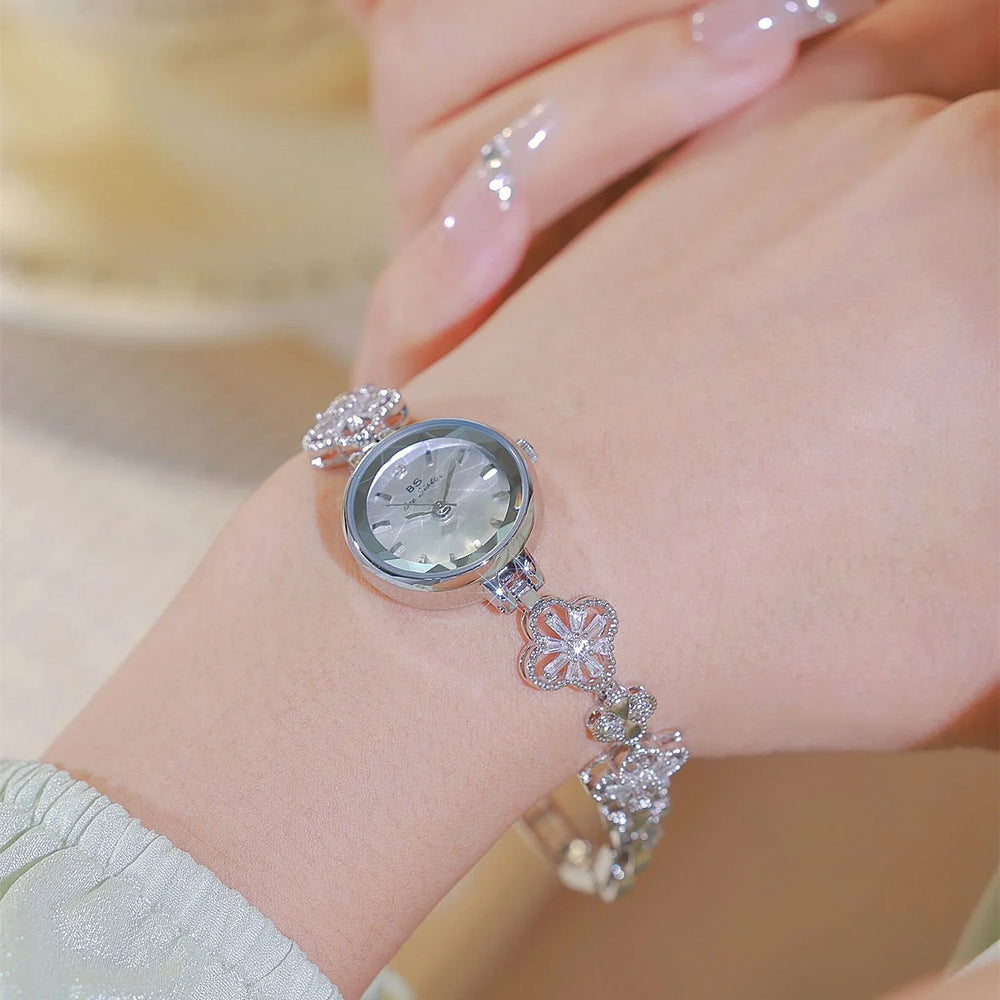 Close-up of a silver floral bracelet watch on a wrist with manicured nails and soft background
