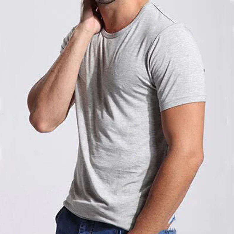 Man wearing plain light gray short sleeve t-shirt paired with blue jeans against a neutral background