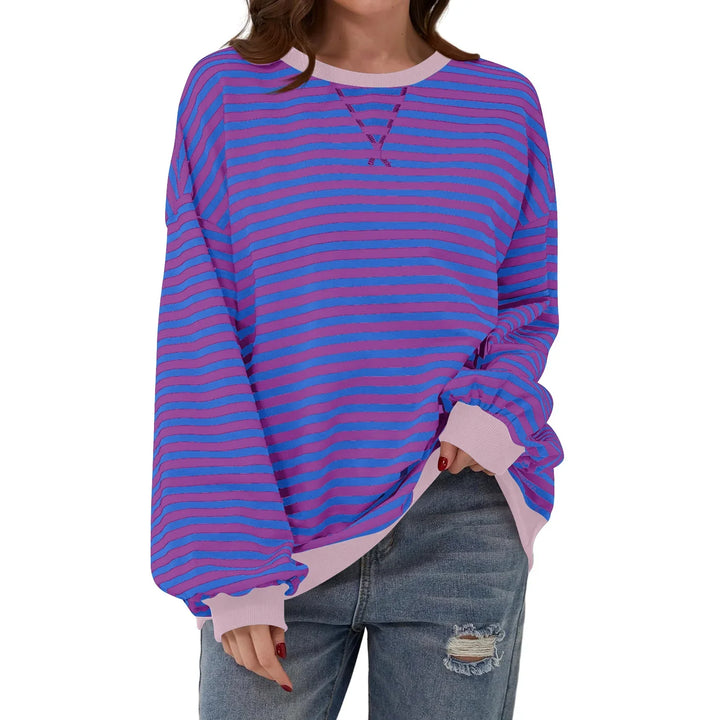 Woman wearing oversized long-sleeve purple and pink striped sweatshirt with ripped blue jeans