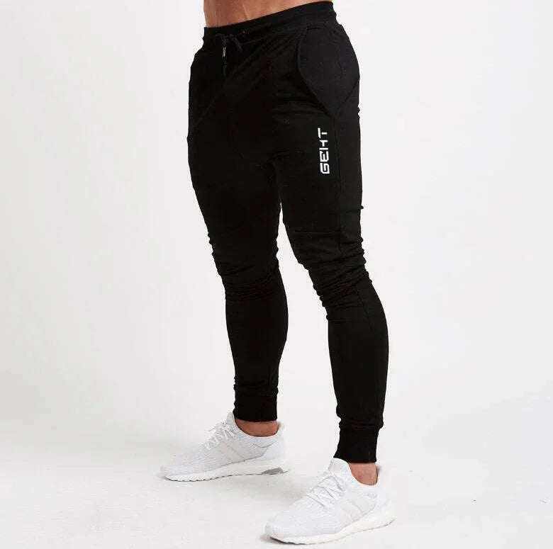Person wearing black slim-fit jogger pants with white logo and white athletic sneakers on white background