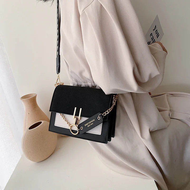 Woman wearing beige dress holding stylish black and beige crossbody handbag with gold chain detail