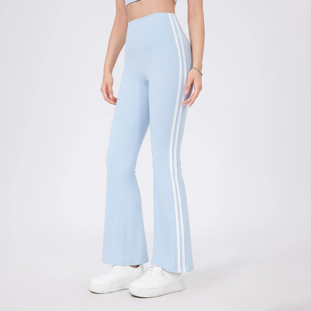 Woman wearing light blue flared leggings with white side stripes and white sneakers on plain background