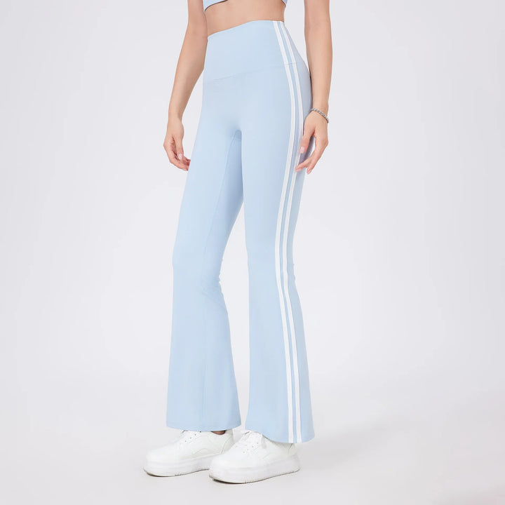 Woman wearing light blue flared leggings with white side stripes and white sneakers on plain background