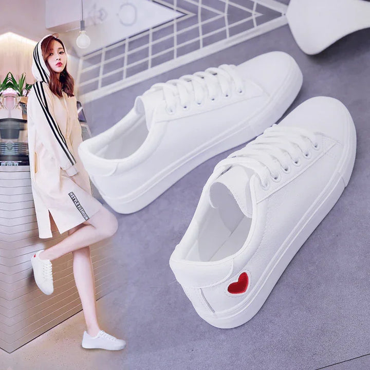 White casual sneakers with red heart detail on gray surface and woman wearing white hooded dress with black stripes