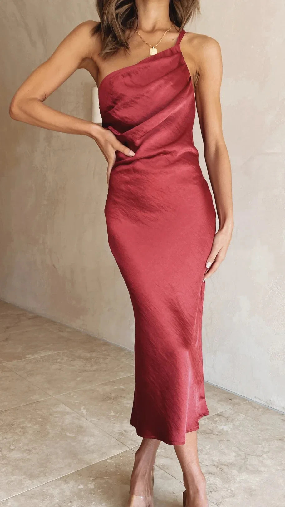 Woman wearing a fitted red satin one-shoulder midi dress with spaghetti strap and gold pendant necklace