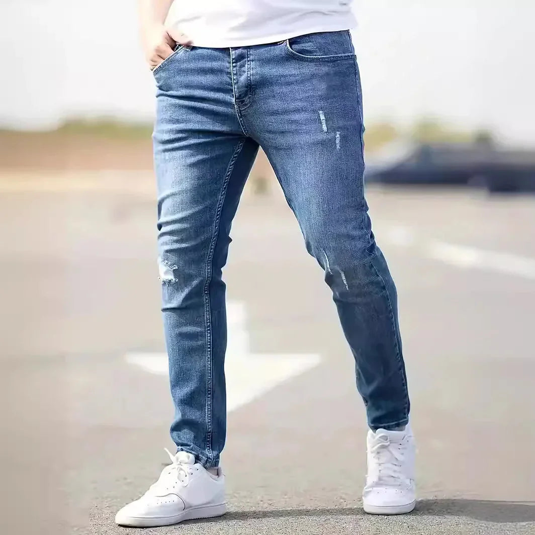 Slim fit blue distressed denim jeans worn with white sneakers on a road background