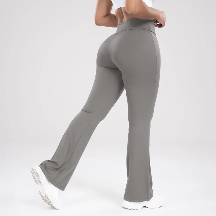 Woman wearing gray high-waisted flare yoga leggings and white sneakers on gray background