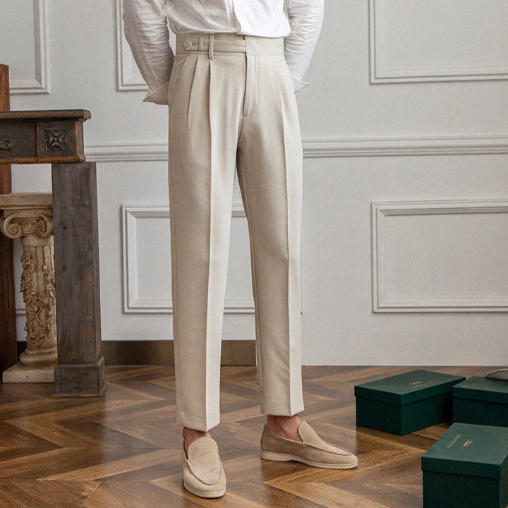 Man wearing beige tailored trousers and loafers standing on wooden floor in elegant room